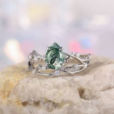 a green ring sitting on top of a rock next to a white crystal stone and diamond accents