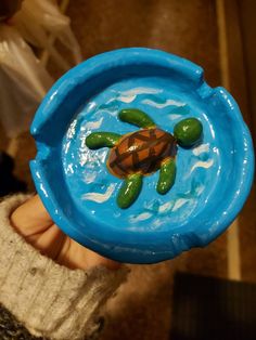 a hand holding a blue plastic bowl with a turtle in it's center and water inside