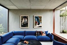 a living room with blue couches and pictures on the wall above it's windows