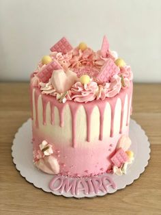 a pink and white cake with icing on a wooden table next to a wall