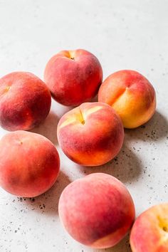 five peaches on a white surface with one sliced in half and the other whole