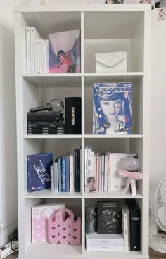 a white book shelf filled with books next to a fan and other items on top of it