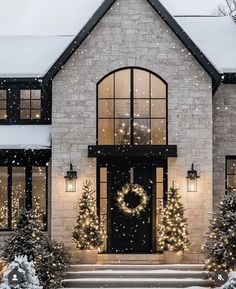 a house decorated for christmas with wreaths and lights on the front door, snow falling all around