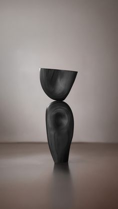 a black vase sitting on top of a wooden table next to a white wall and floor