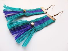 two pairs of earrings with tassels are shown on a white surface, one is blue and the other is green