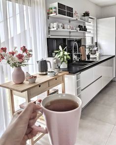 a person holding a cup of coffee in their hand while sitting at a kitchen table