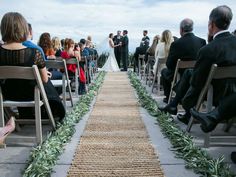 an outdoor ceremony with people sitting on chairs and one man standing at the end of the aisle