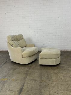 a white chair and ottoman sitting next to each other on a cement floor in front of a brick wall