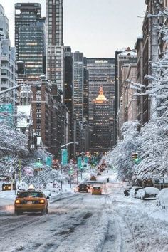 cars driving down a snow covered street in the middle of tall buildings and skyscrapers