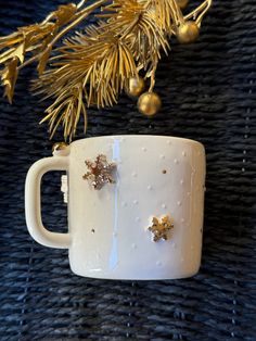 a white mug with gold stars on it next to a pine branch and christmas decorations