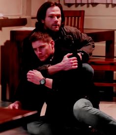 two men sitting on the floor with their arms around each other and one man holding his arm