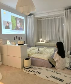 a woman sitting on the floor in front of a bed with a projector screen