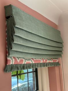 a green roman blind hanging from the side of a window in a pink room with an open window