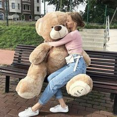 a woman sitting on a bench hugging a large teddy bear