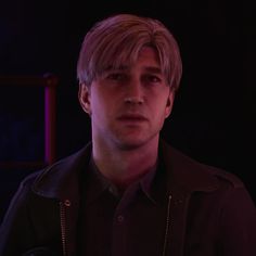 a young man with blonde hair wearing a black shirt and leather jacket in the dark