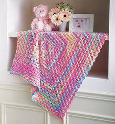 a pink teddy bear sitting on top of a shelf next to a crocheted blanket