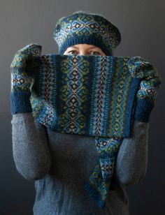 a woman wearing a knitted hat and scarf with her hands in the air, covering her face