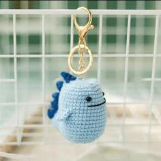 a crocheted blue fish keychain hanging from a metal hook in a cage