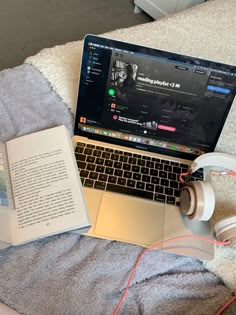 an open laptop computer sitting on top of a bed next to headphones and books