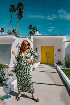 a woman standing in front of a yellow door wearing a green and white floral dress