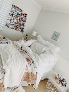 an unmade bed with many pictures on the wall above it and a small side table