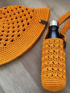 an orange crocheted bag with a water bottle in it sitting on the floor