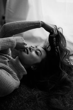 a black and white photo of a woman laying on the floor with her hair pulled back