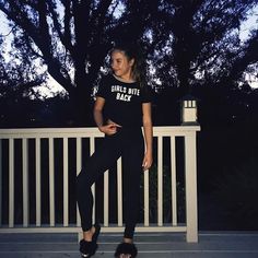 a woman sitting on top of a white bench next to a tree and wearing black sandals