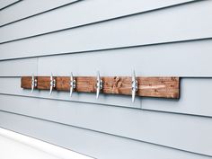 a wooden coat rack on the side of a house with five coats hanging from it