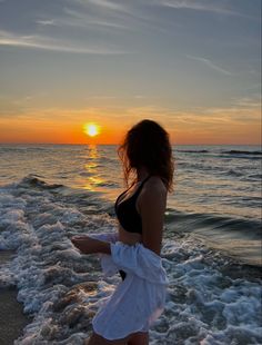 a woman standing on top of a sandy beach next to the ocean at sunset or dawn