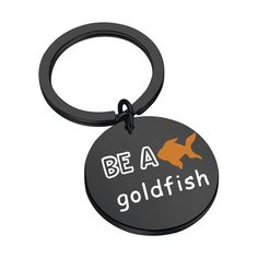 a black round keychain with an orange fish on it that says be a goldfish