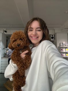 a woman holding a brown dog in her arms and smiling at the camera while wearing a white sweater