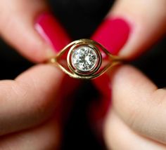 a woman's hand holding a gold ring with a diamond in the middle and red nail polish