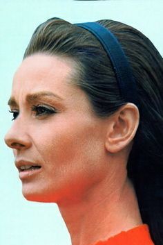 a woman in an orange top with her hair pulled back and wearing a black headband