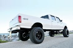 a white truck parked on top of a road next to the ocean in front of some rocks