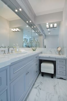 a large bathroom with marble counter tops and gray cabinets, along with white stools