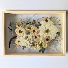 an arrangement of flowers in a wooden frame on a white wall behind a shadow box