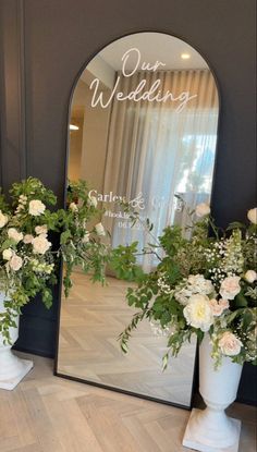 two white vases with flowers in front of a large mirror on the floor next to each other