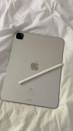 an ipad with a pencil on top of it sitting on a white sheet covered bed