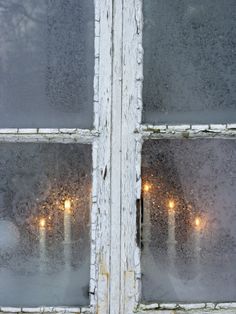 candles are lit behind frosted glass in an old window