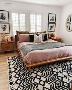 a bed with pink sheets and pillows in a bedroom next to two framed pictures on the wall