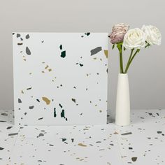 two white roses in a vase next to a card on a table with confetti sprinkles