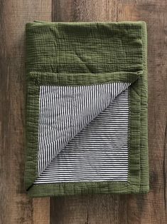 a green and black striped blanket on top of a wooden floor next to a piece of wood