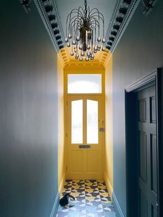 an empty hallway with a yellow door and chandelier hanging from it's ceiling