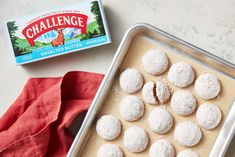 a pan filled with snowball cookies next to a carton of challenge powdered sugar