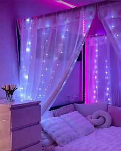 a purple bedroom with white curtains and pink lights on the walls, along with a bed covered in fluffy pillows