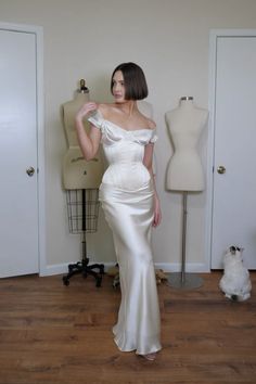 a woman in a white dress standing next to a mannequin and a cat