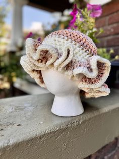 a close up of a hat on a mannequin head with flowers in the background