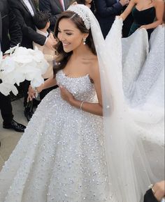 a woman in a white wedding gown and veil is walking through the crowd with other people