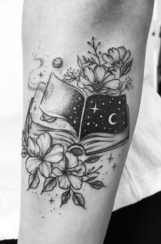 a black and white photo of a book with flowers on the cover up, next to a crescent moon